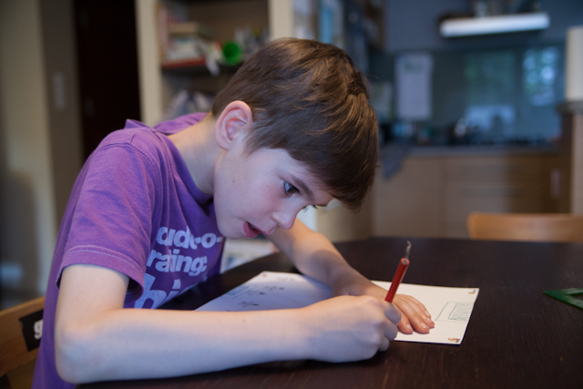 Ein Junge sitzt am Tisch und zeichnet mit dem Bleitstift mit einem angestrengtem Gesicht