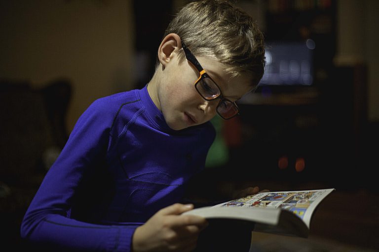 Ein blondhaariger Junge mit Brillen beim Lesen von einem Comic-Buch