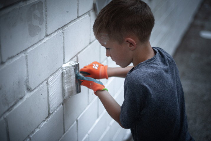Ein blondhaariger Junge streicht eine Wand mit der weissen Farbe