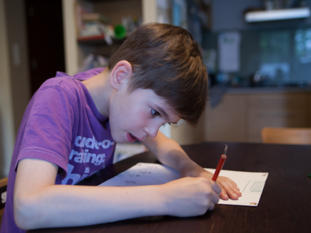 Ein Junge sitzt am Tisch und zeichnet mit dem Bleitstift mit einem angestrengtem Gesicht